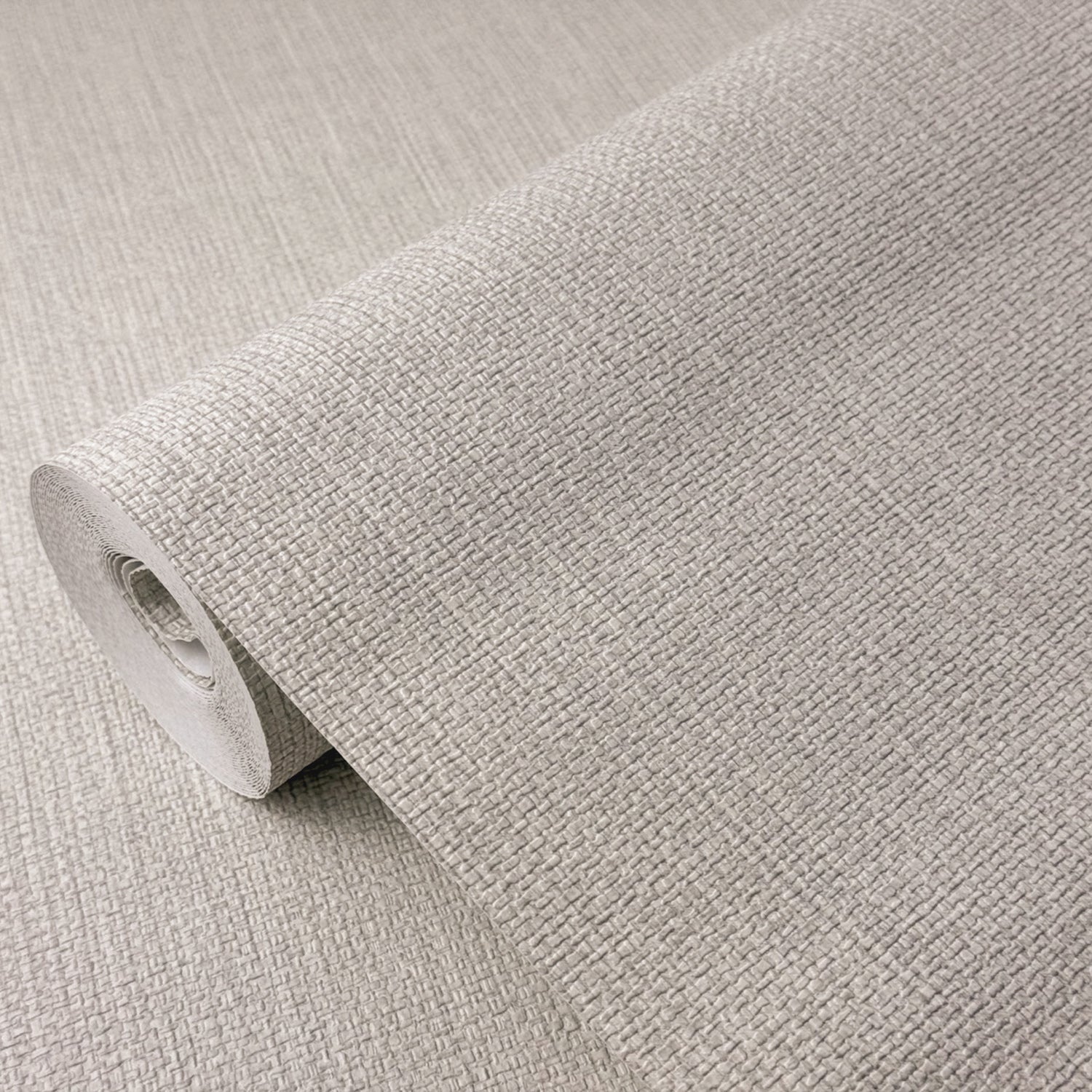A close-up of a rolled sheet of textured wallpaper in a light warm gray or greige tone, showing the woven fabric-like pattern and adhesive backing.