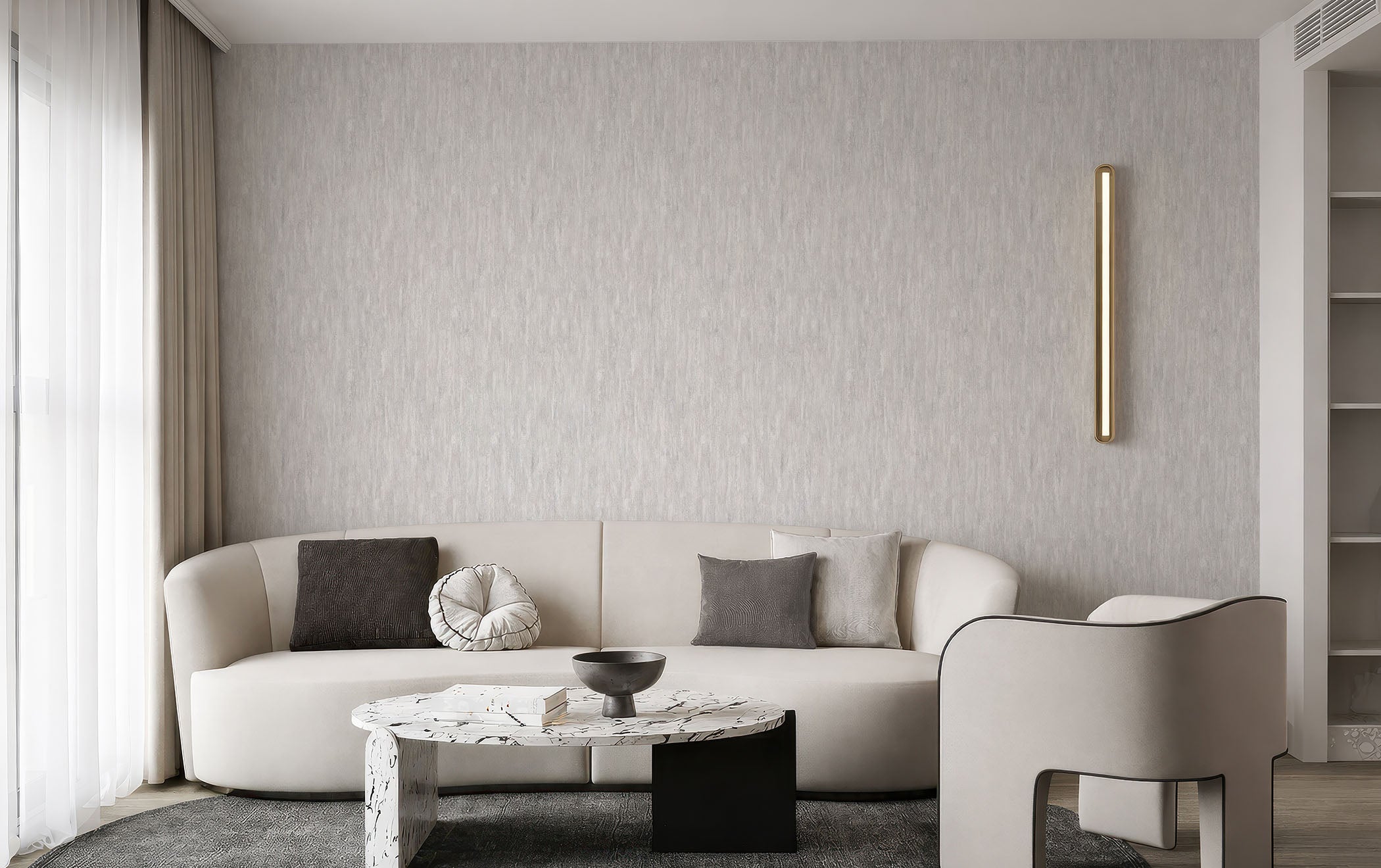 A modern living room featuring a textured light gray wall, a curved white sofa with dark and gray pillows, a marble-top coffee table, and a light gray armchair.